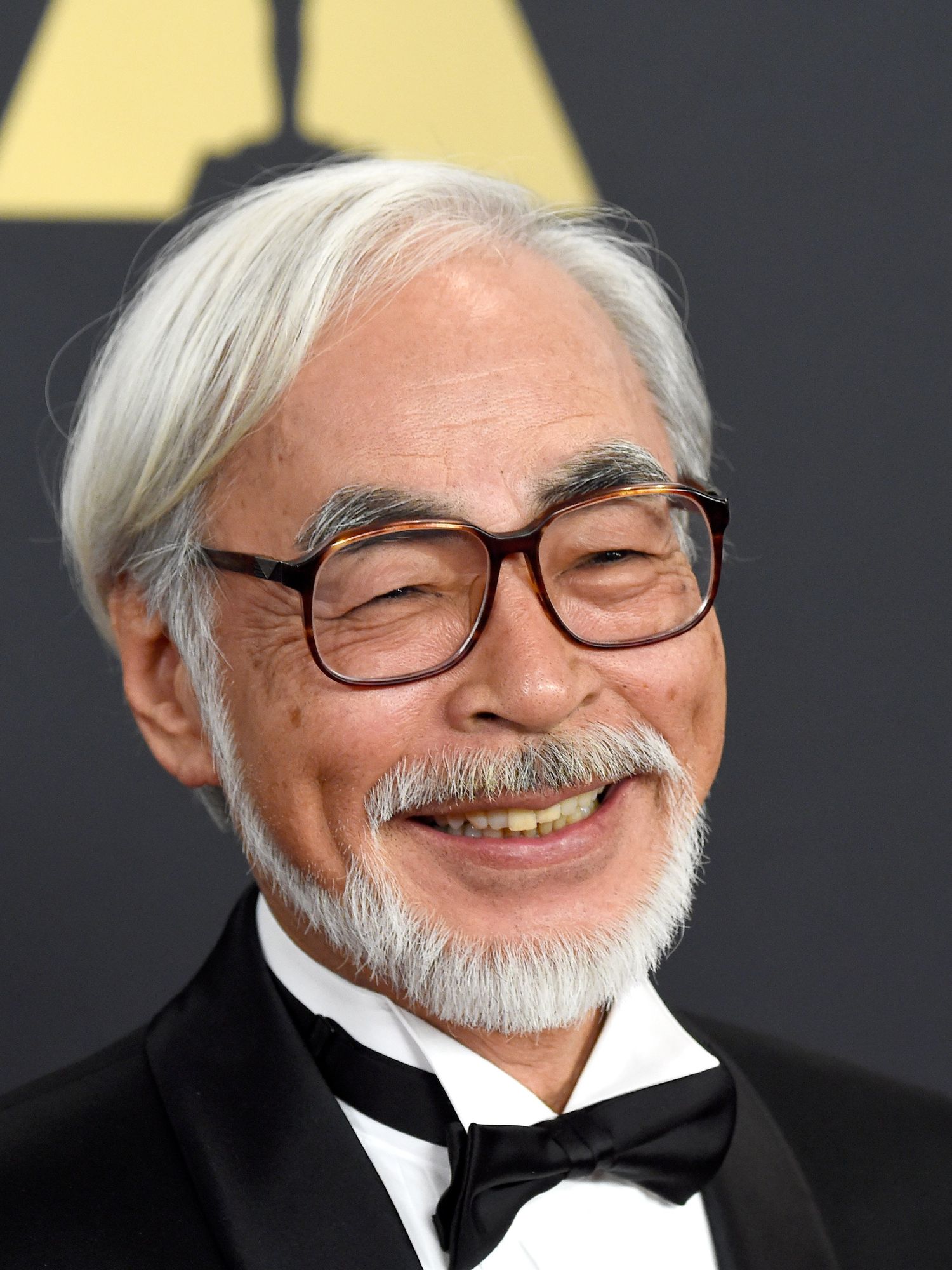 Hayao Miyazaki, a Japanese man with white hair, a beard and glasses, smiles at an Academy event.
