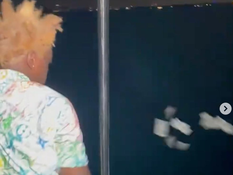 He is seen picking up the remaining $100 bills off the floor and throwing them into the sea