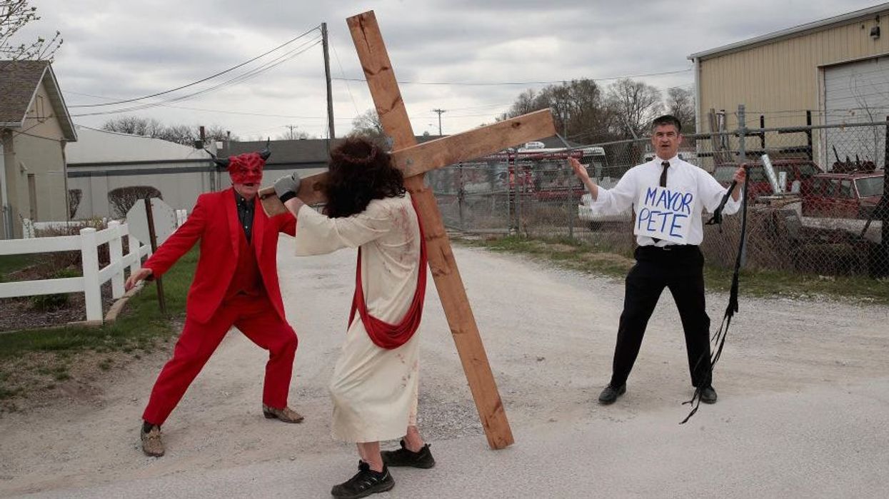 Homophobic protester dresses as Pete Buttigieg and whips Jesus on the cross at political rally while devil cheers him on