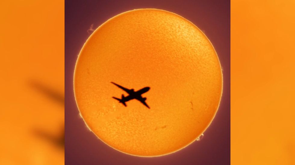 Aeroplane seen silhouetted dramatically in front of the Sun as it crosses perfectly across the fiery surface