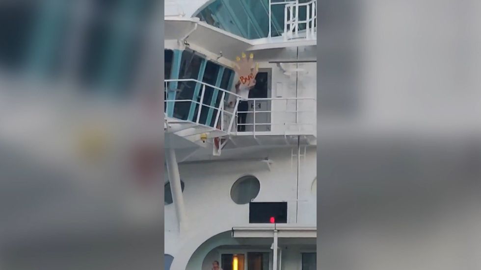Crew member waves with giant foam hand as cruise ship leaves stranded passengers behind