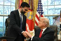In the Oval Office, Zohran Mamdani, standing left, shakes the hand of Donald Trump, sitting down in a black chair behind his desk.