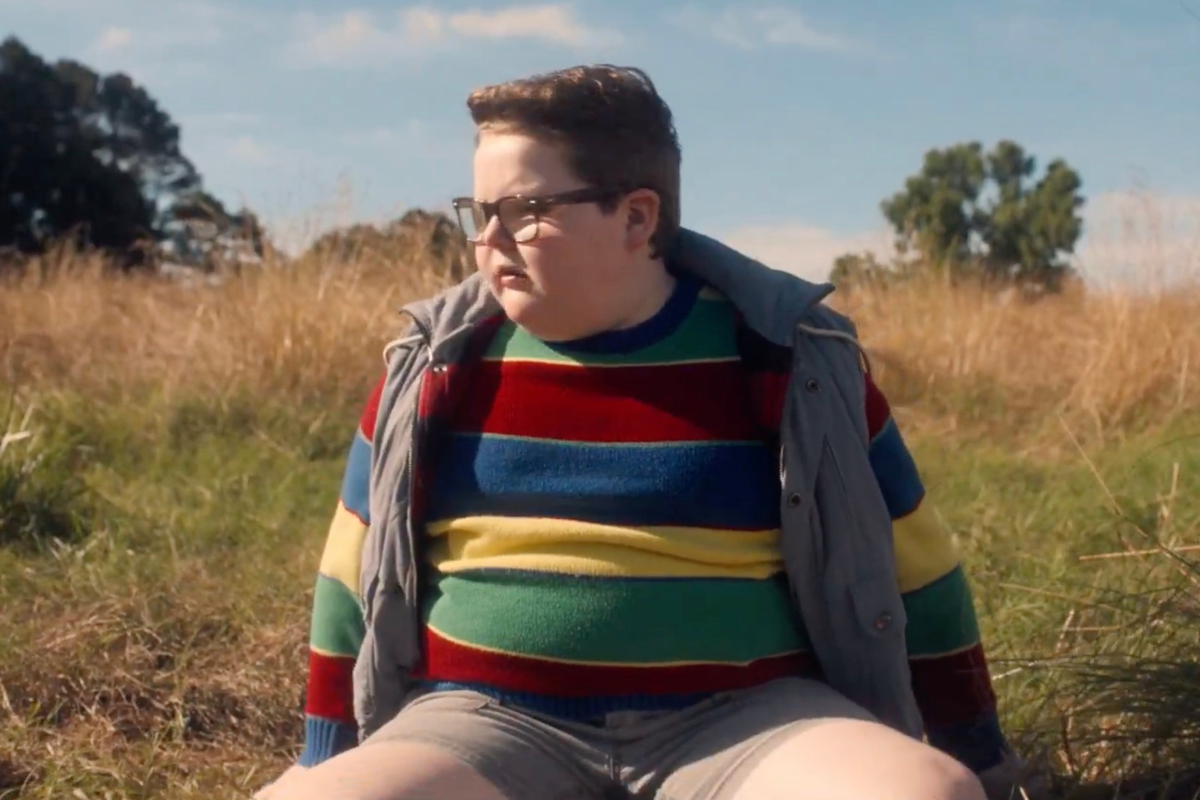 Jake Connelly as Derek Turnbow in Stranger Things. He is looking to his right, confused, sitting in a field.