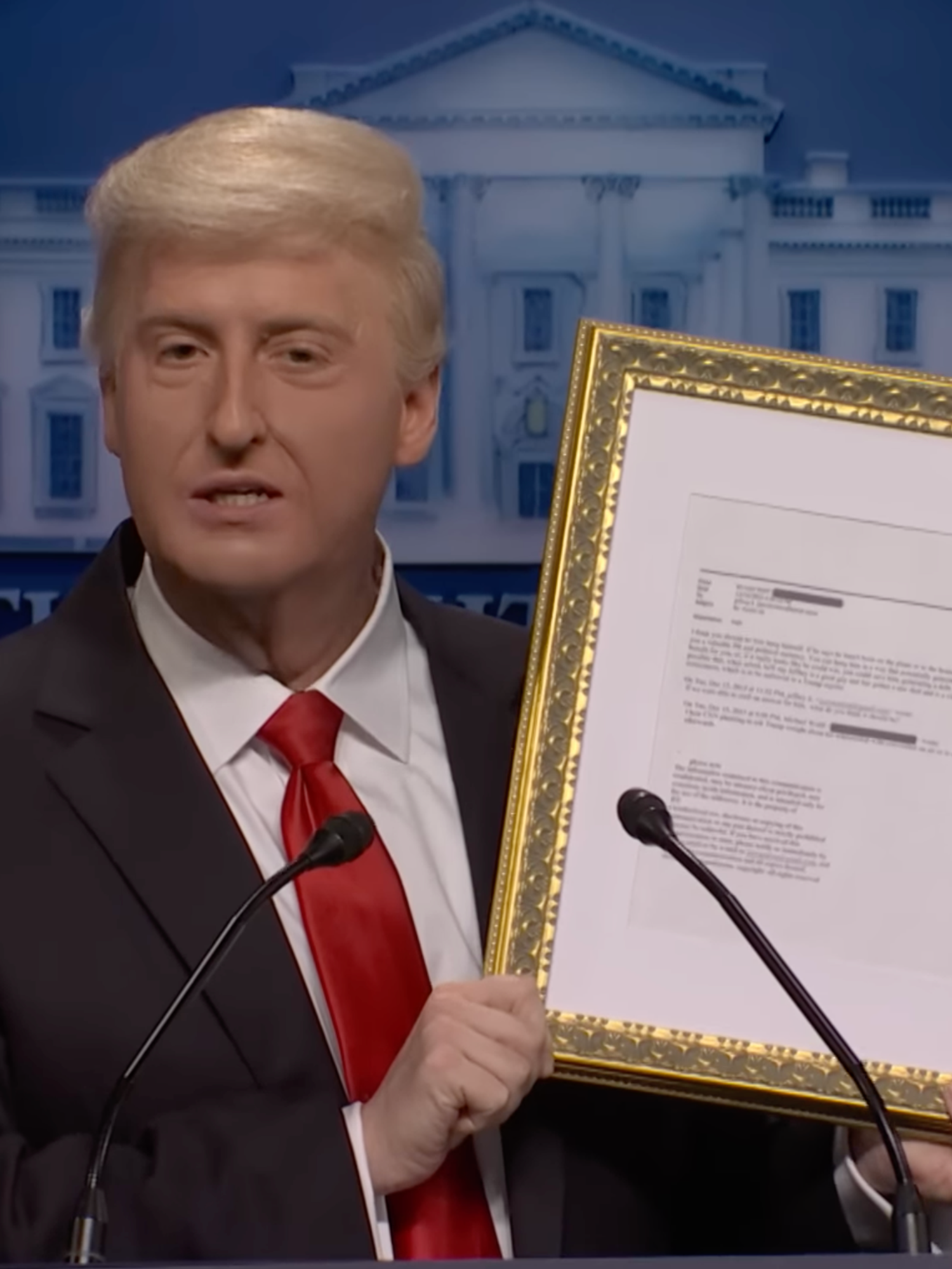 James Austin Johnson as Donald Trump speaking in front of a presidential lectern and holding up a gold-framed copy of an Epstein email.