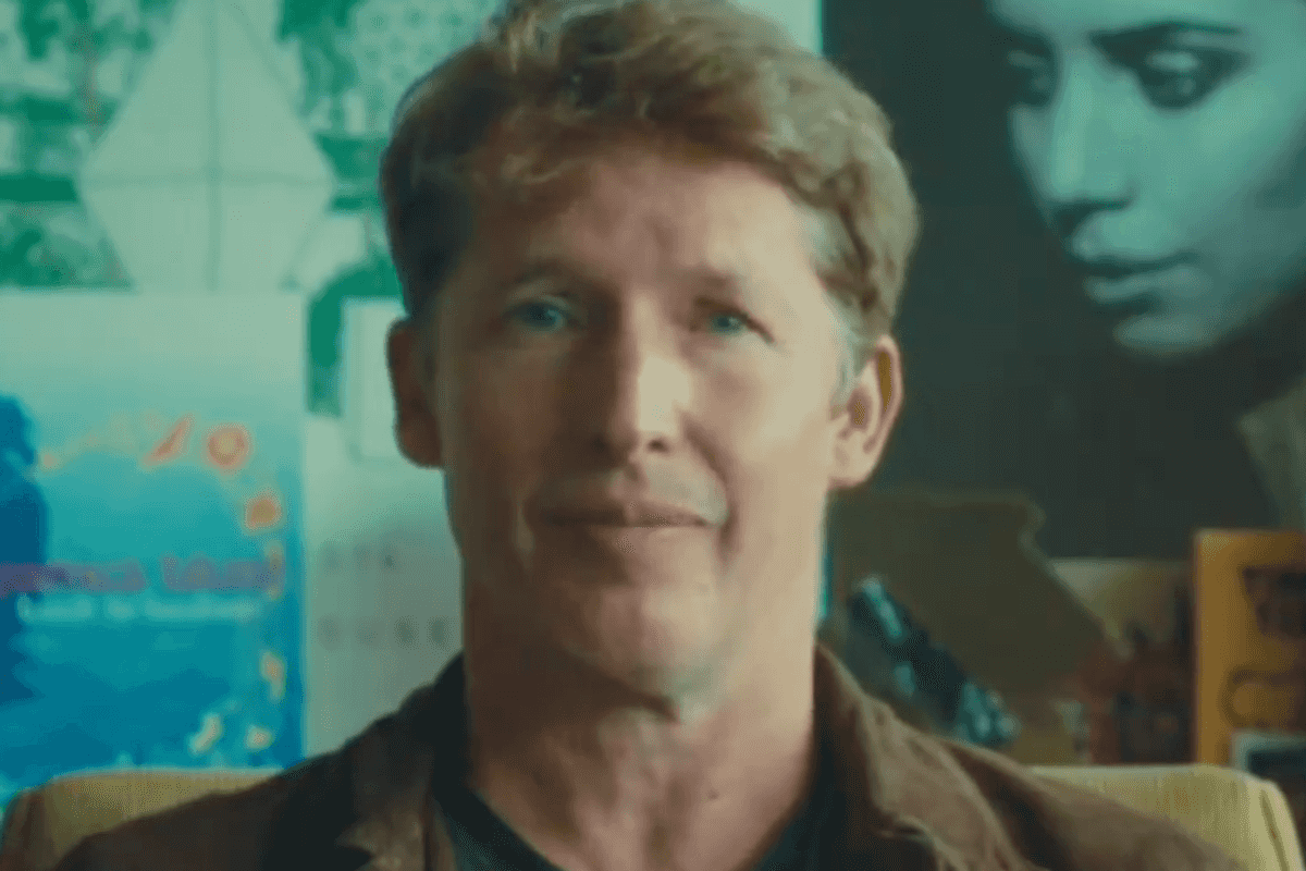 James Blunt gives a gentle smile to the camera, with album covers on a wall behind him.