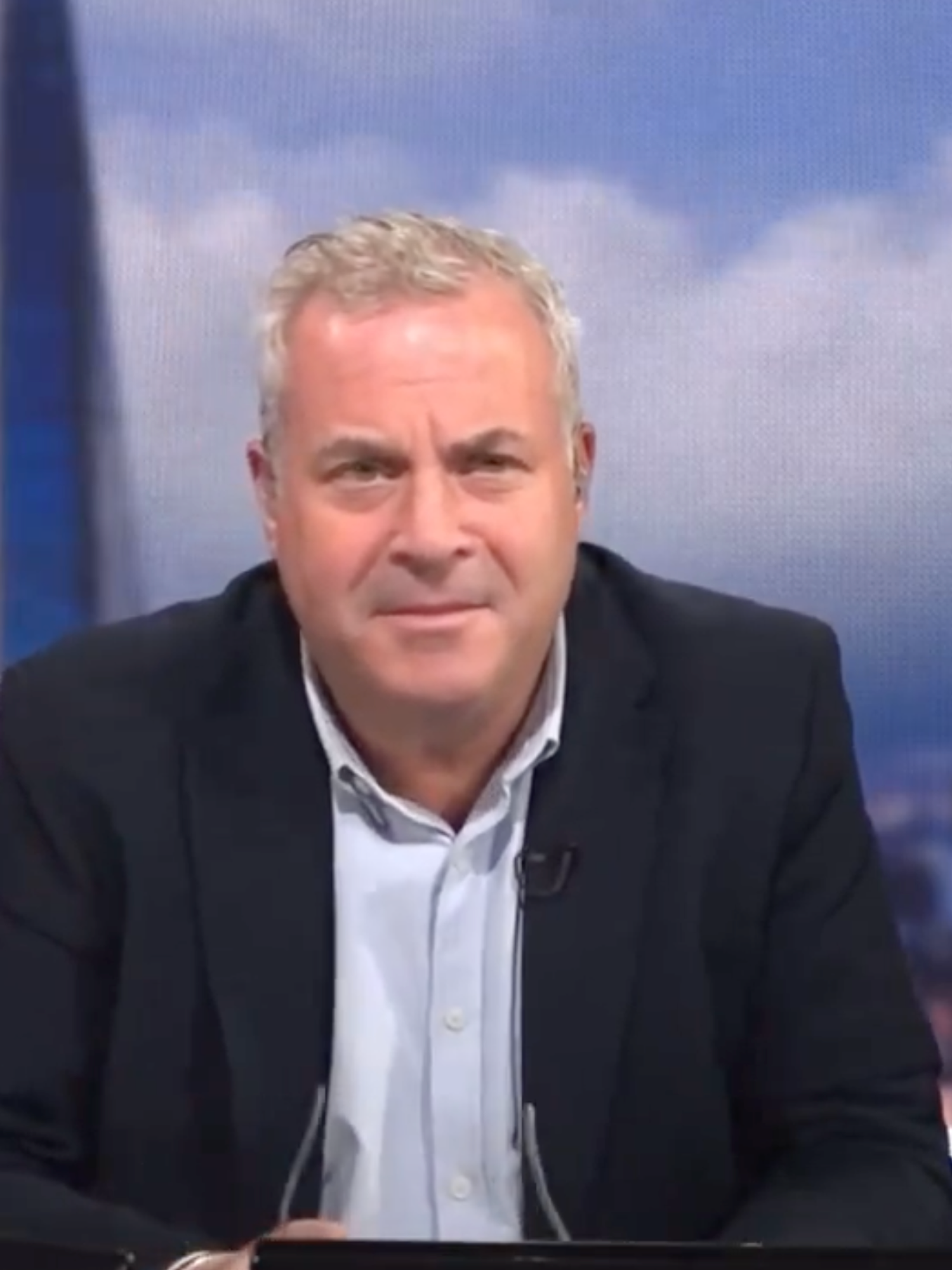 James Max, a white man in a black suit jacket with short grey hair, presenting a show on TalkTV.