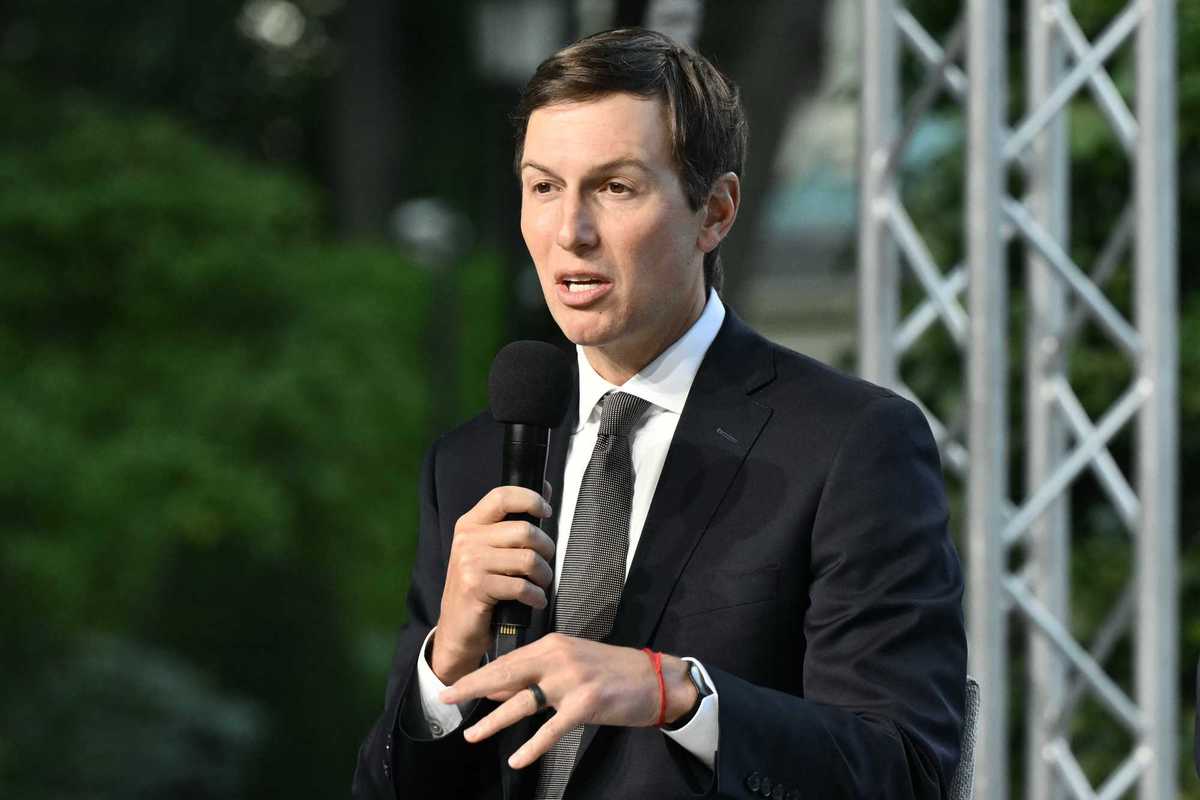 Jared Kushner, a white man with short black hair and a black suit, speaking into a microphone on-stage.