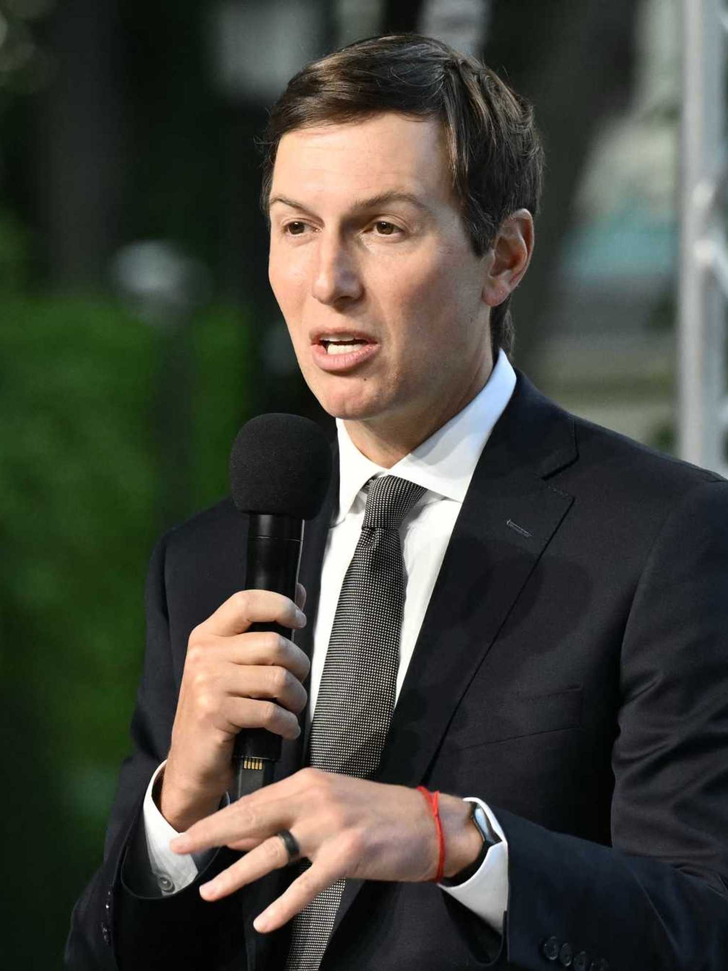 Jared Kushner, a white man with short black hair and a black suit, speaking into a microphone on-stage.