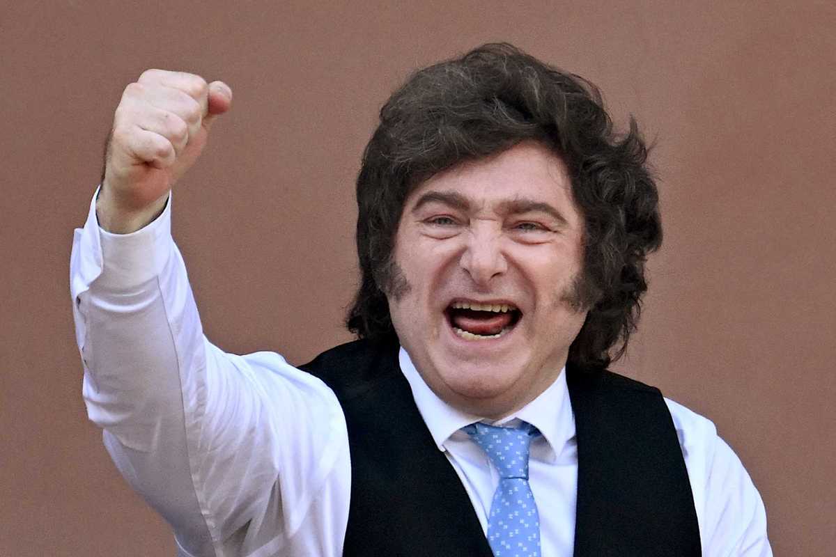 Javier Milei, a white man with long, curly black hair, smiles and punches the air with his right fist.
