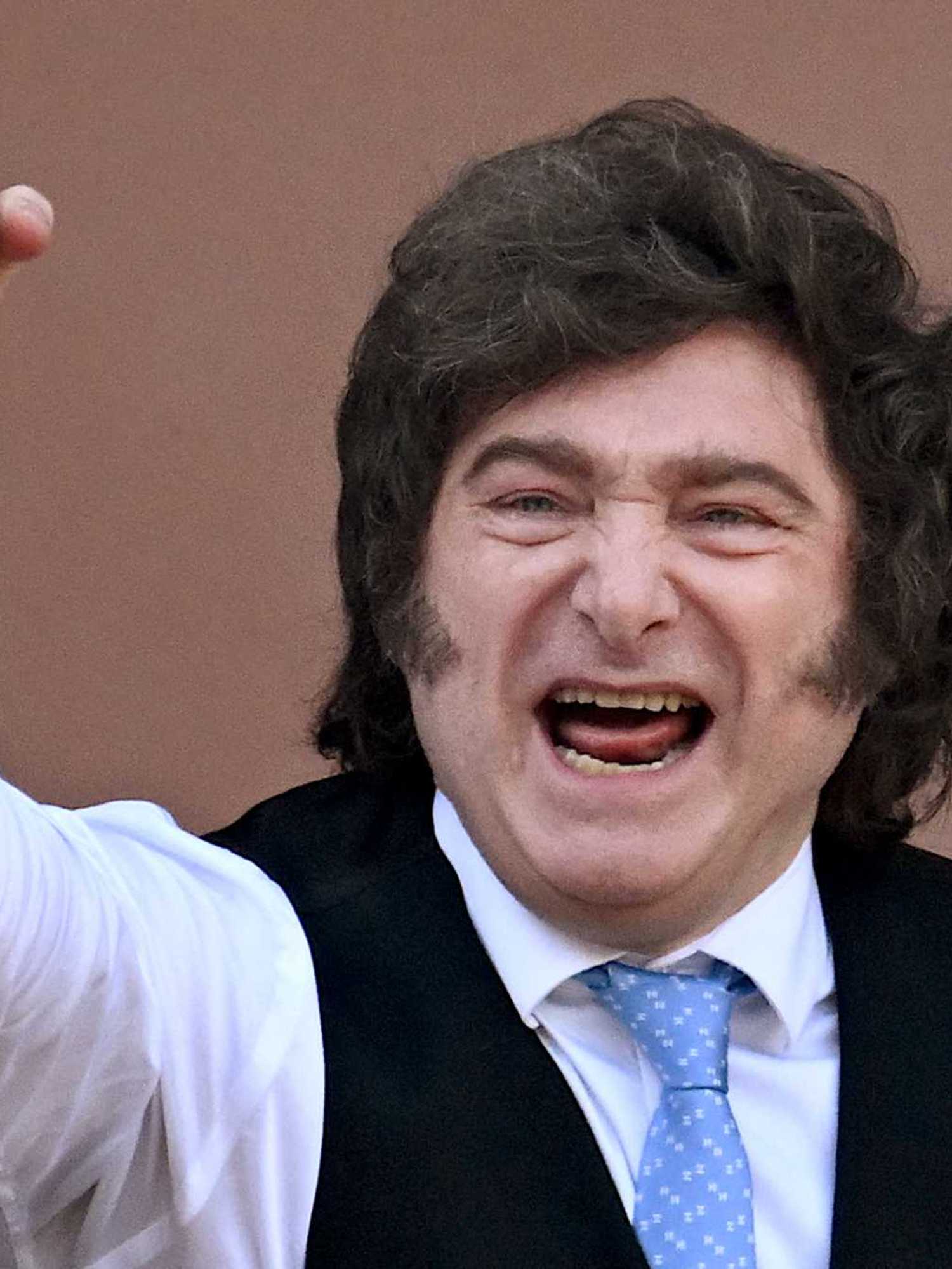 Javier Milei, a white man with long, curly black hair, smiles and punches the air with his right fist.