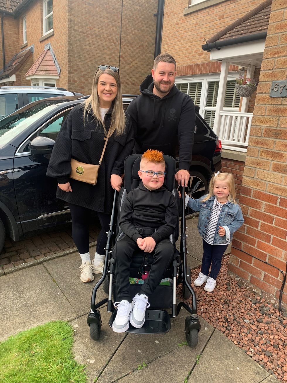 Jaxon in a wheelchair, smiling alongside his mother, father and sister
