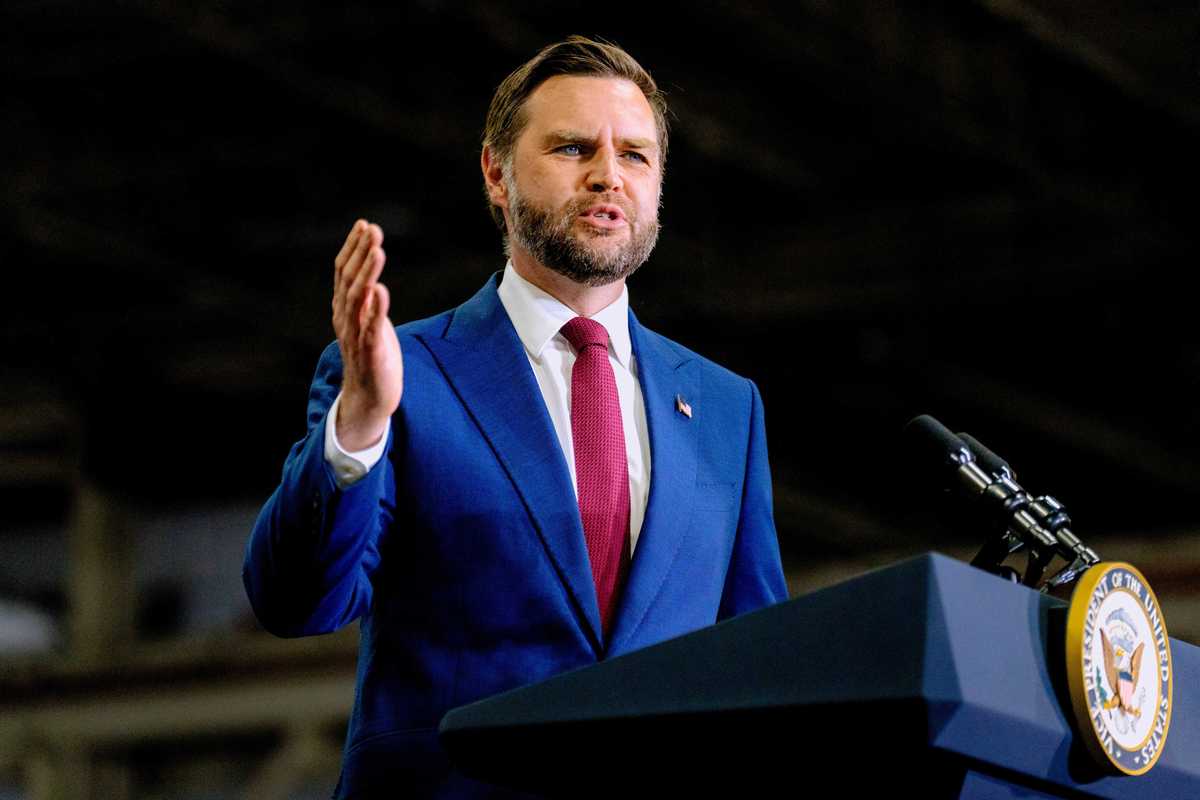 JD Vance in a blue suit speaks behind a dark blue vice presidential podium.