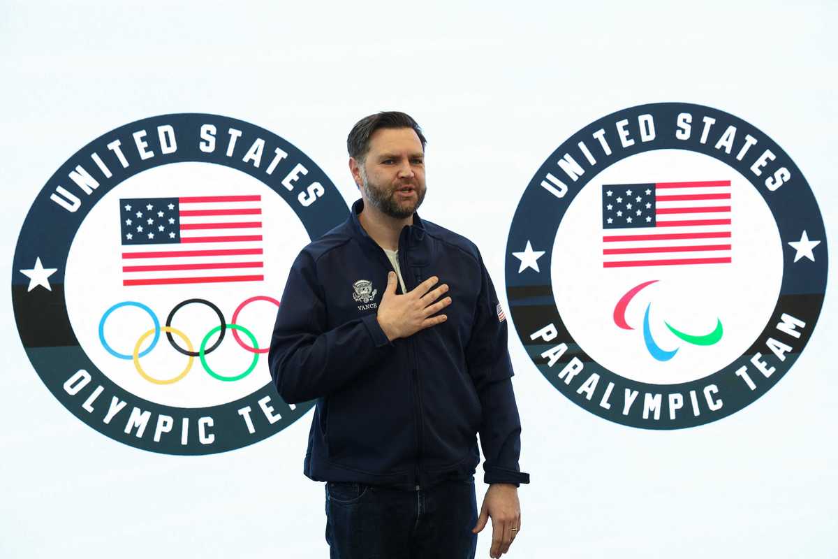 JD Vance places hand on chest as he stands in front of signage for the United States Olympic and Paralympic teams.