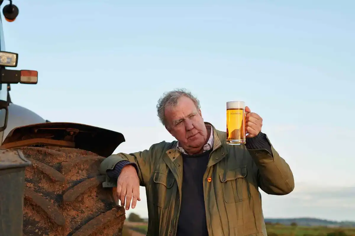 Jeremy Clarkson leans on a tractor and poses with a pint of beer
