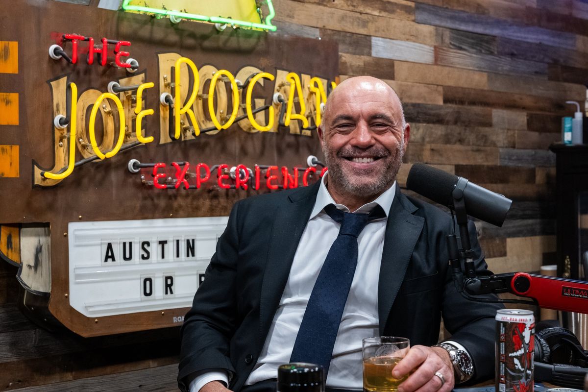 Joe Rogan sits in front of a sign advertising his podcast