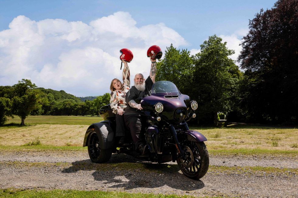 John and Lucy Waring on a motor bike waving their helmets in the air
