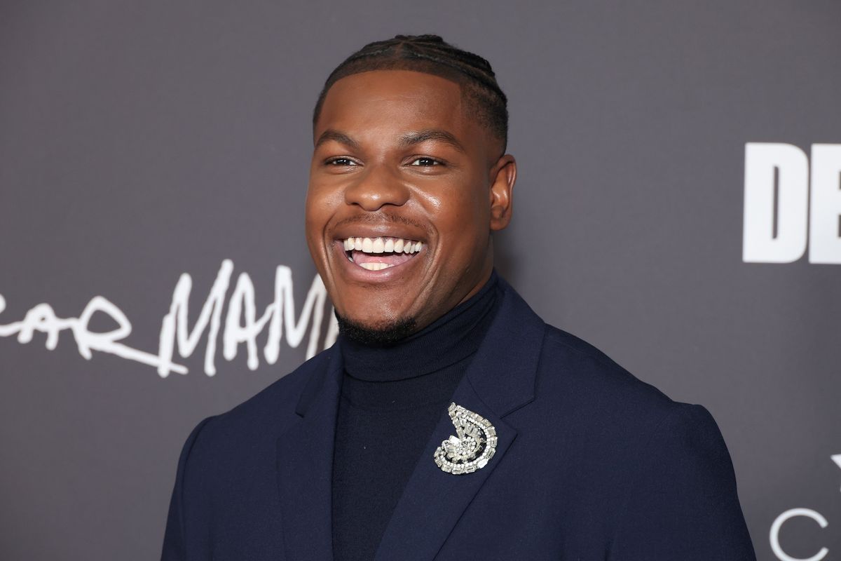 John Boyega wears a blue suit and turtleneck jumper as he smiles at the Critics Choice Association celebration