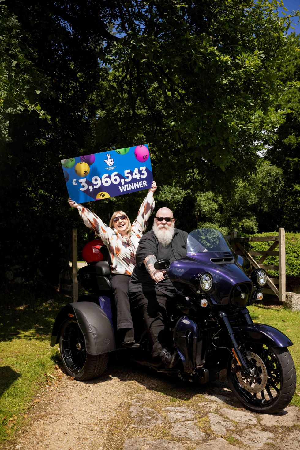 Jon and Lucy Waring on a motorbike with Lucy holding a National Lottery winner's placard