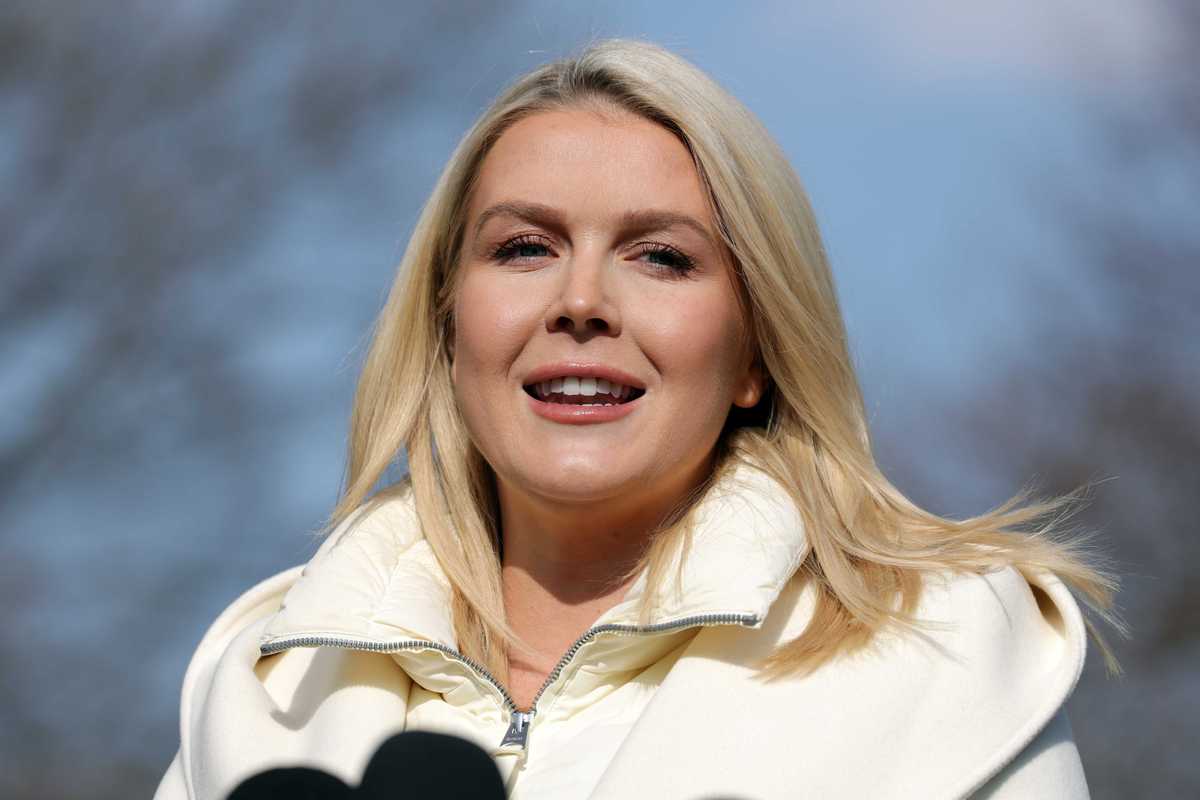 Karoline Leavitt, a white woman with long blonde hair and a white coat, standing outside the White House.
