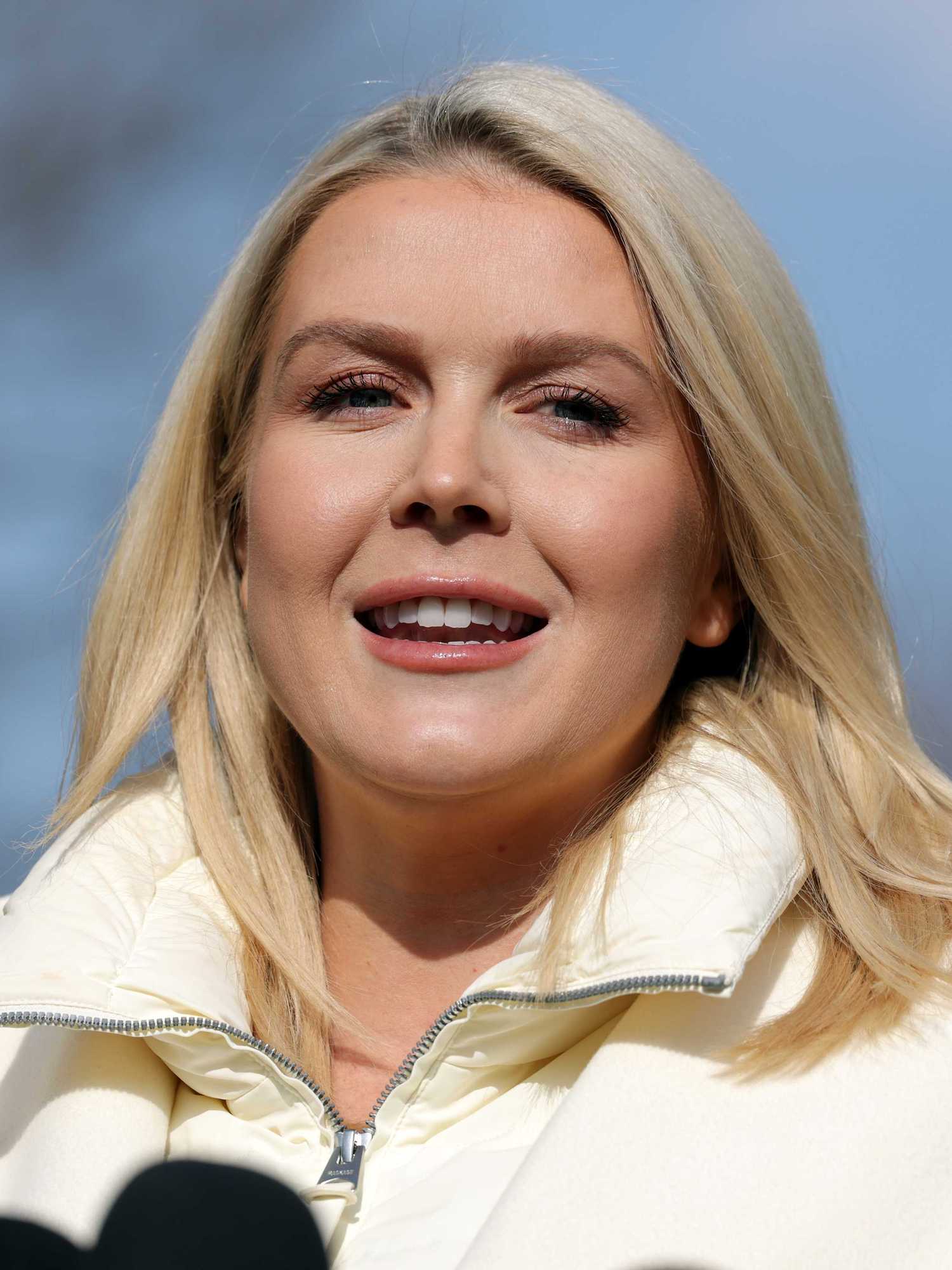 Karoline Leavitt, a white woman with long blonde hair and a white coat, standing outside the White House.
