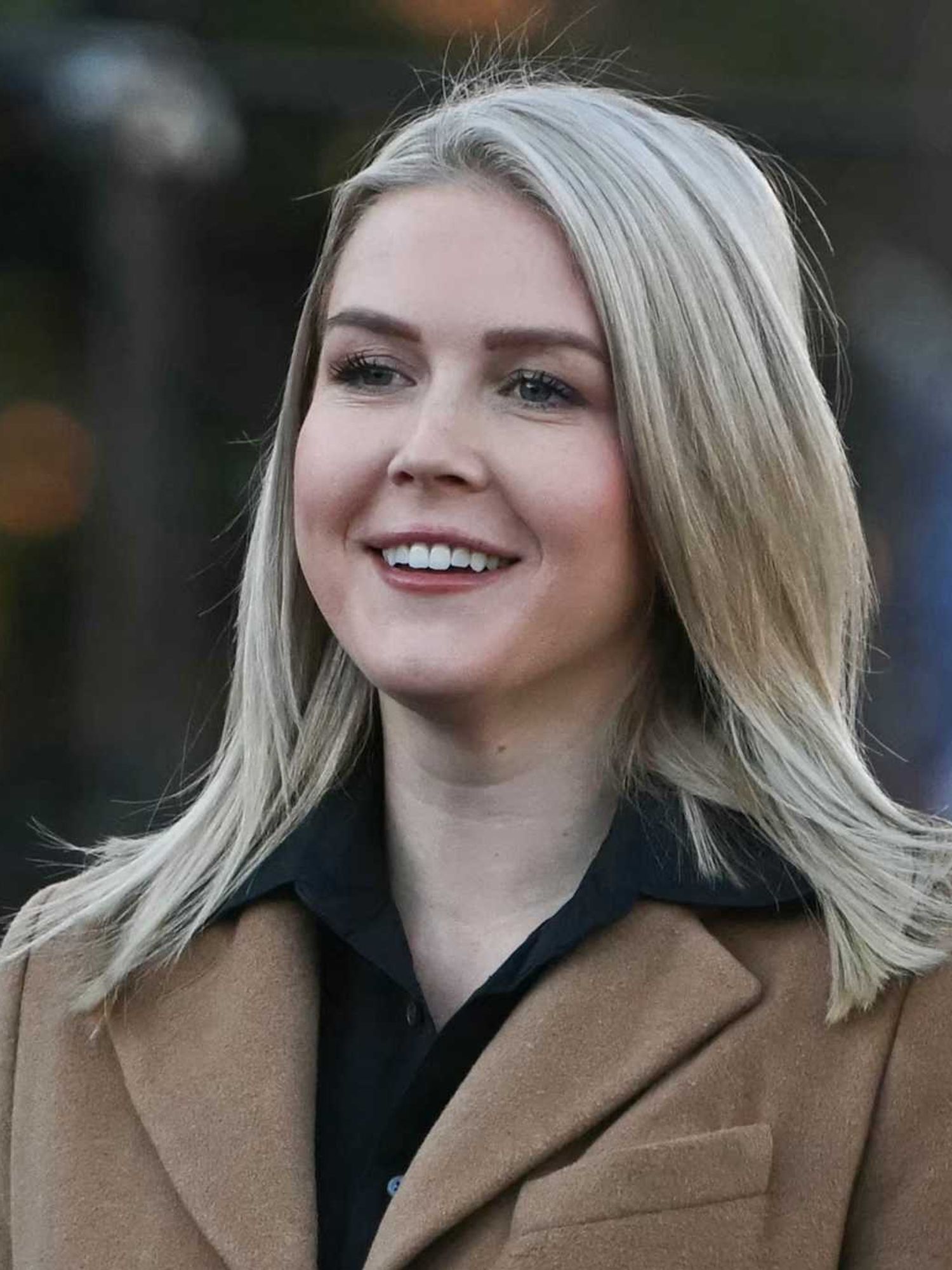 Karoline Leavitt, a white woman with short blonde hair and a brown coat, smiling.