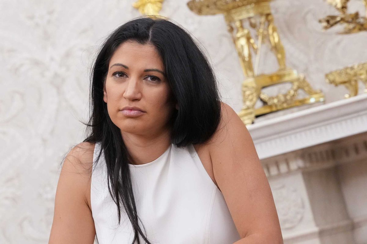 Katie Miller, a white woman with long black hair and a white vest top, sitting in the White House.