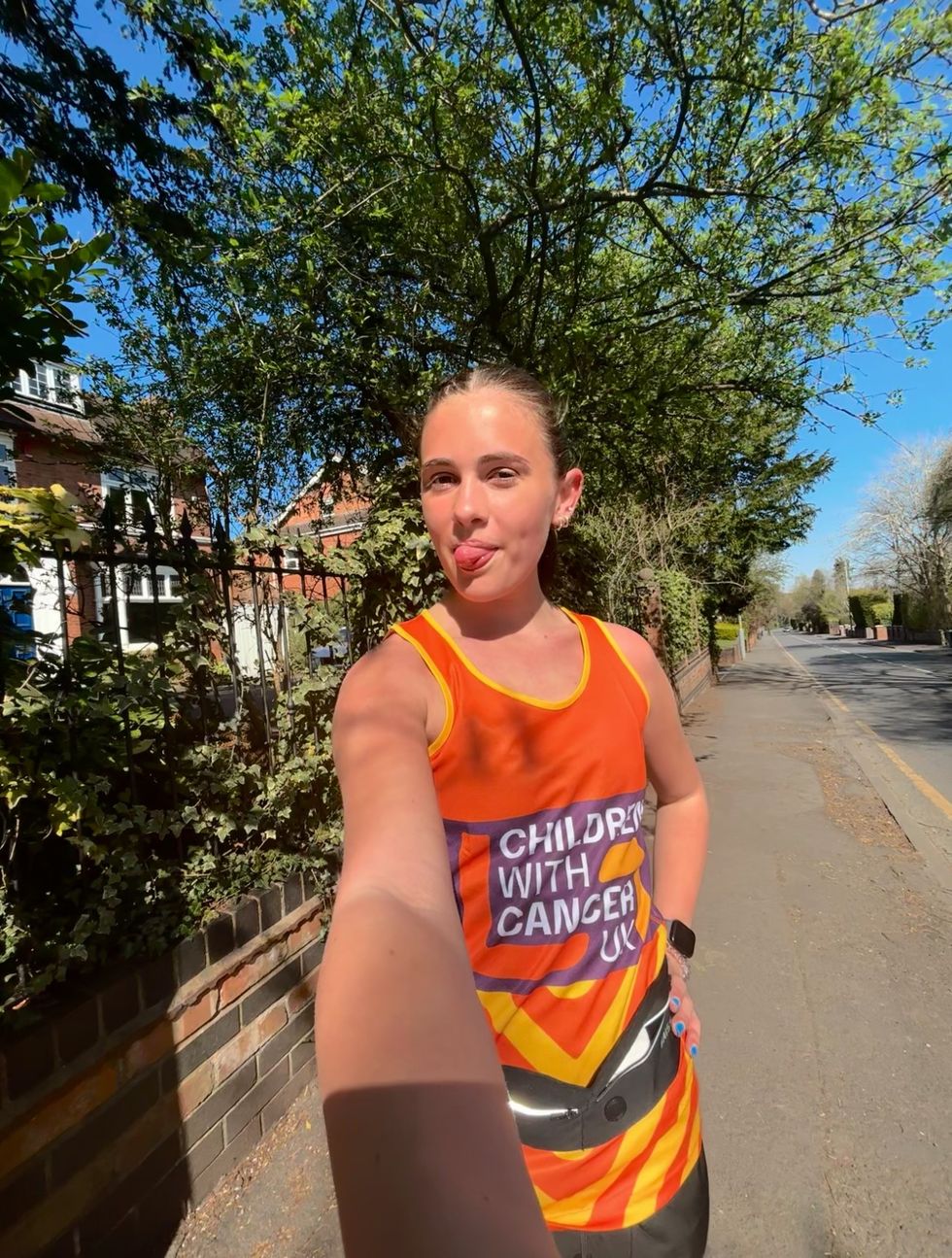 Katies Oates poking out her tongue while wearing a Children with Cancer UK orange running vest