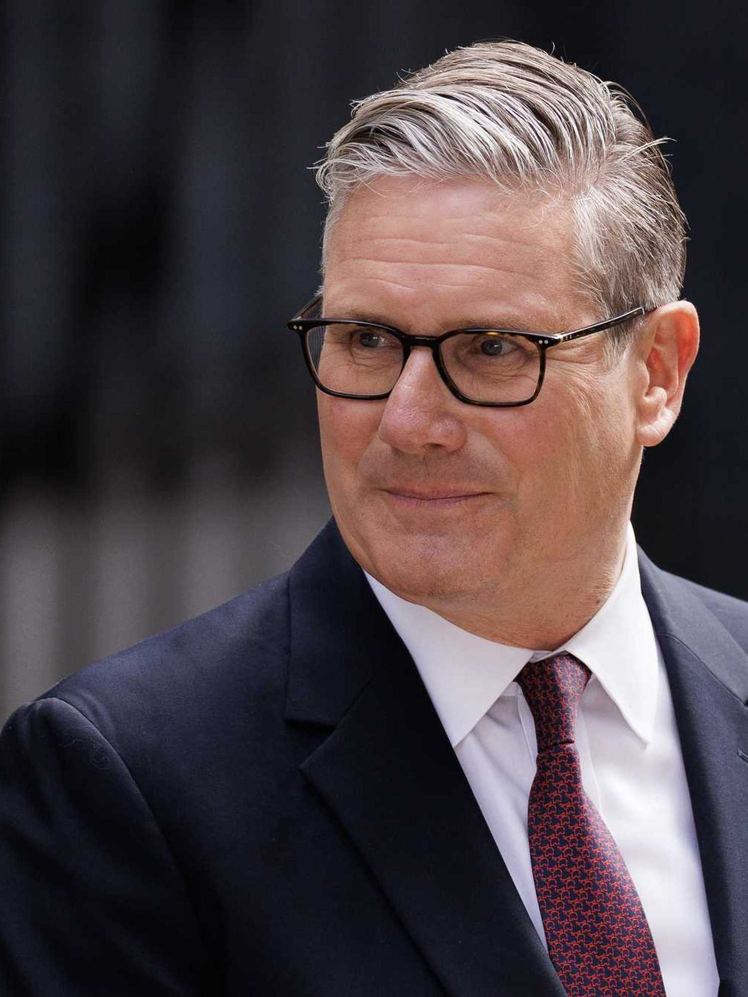 Keir Starmer looks to his right and smiles while standing outside Number 10.