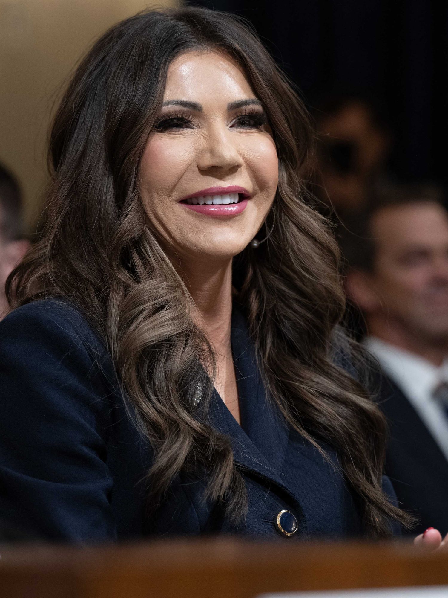 Kristi Noem, a white woman with wavy brown hair, smiles as she answers questions during a committee hearing.