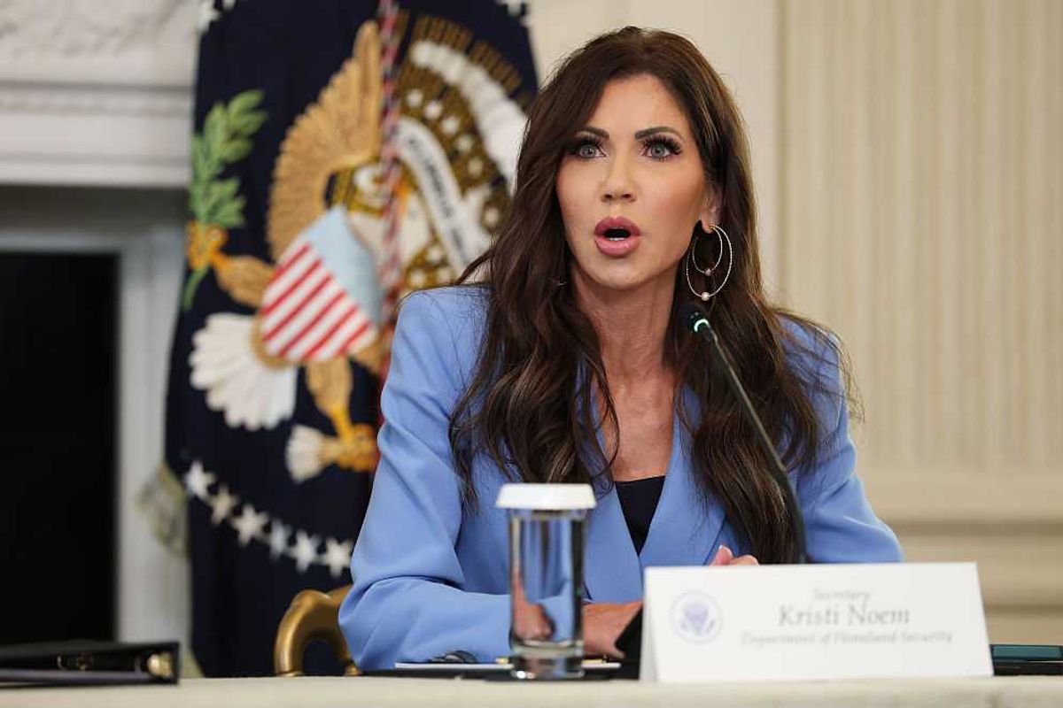 Kristi Noem sits behind a white desk wearing a light blue suit jacket.