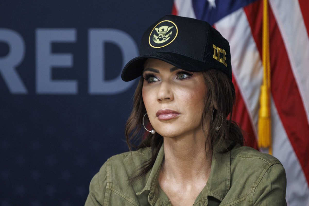 Kristi Noem, wearing a green collared shirt and black and gold ICE cap.