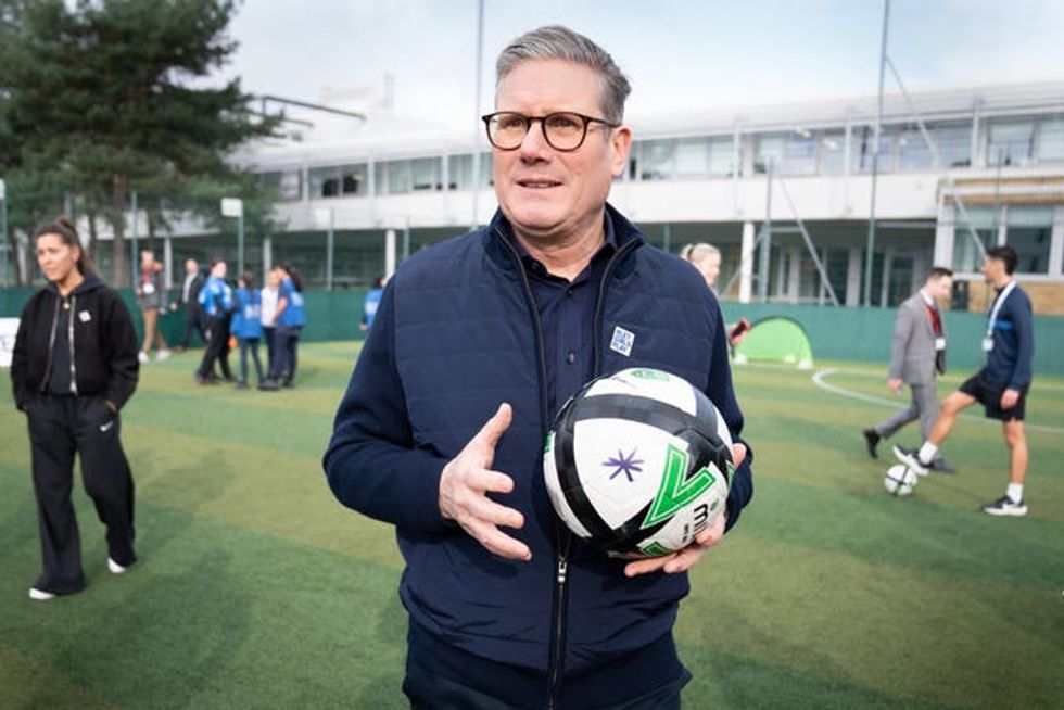 Labour leader Keir Starmer stands on astroturf holding a white and black football