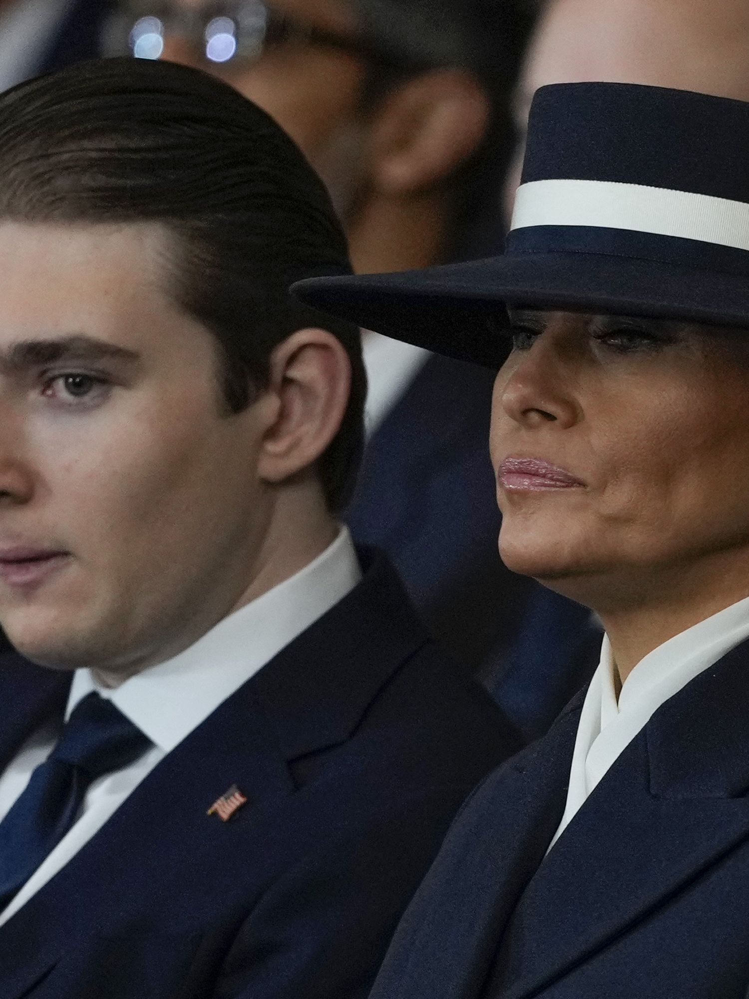 Left, Barron Trump, and right, Melania Trump. Both in black clothing, with Melania wearing a black hat, at Donald Trump's inauguration.