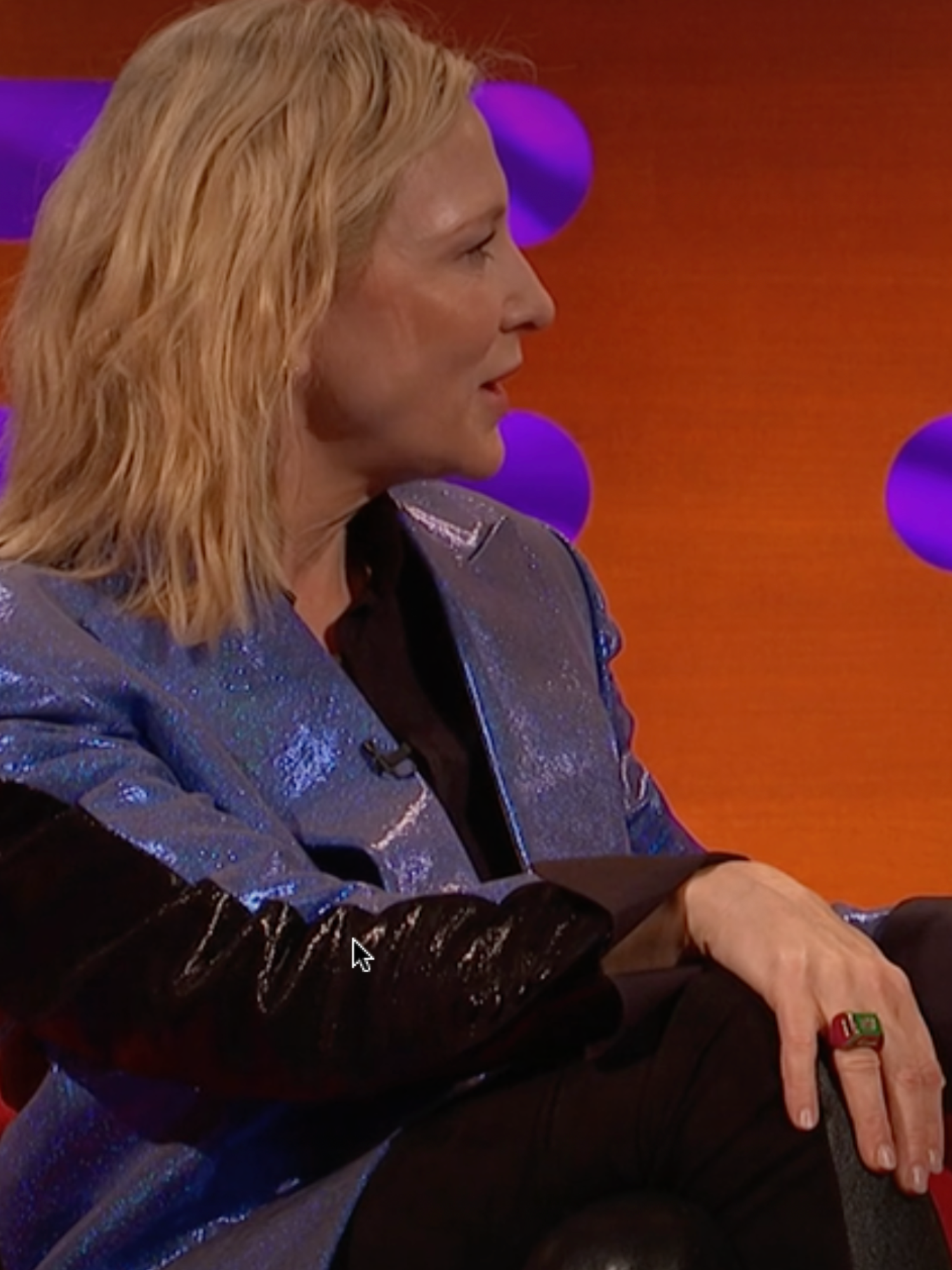 Left, Cate Blanchett, a white woman with short blonde hair and a shiny blue jacket. Right, Margot Robbie, a white woman with short brown hair and a mustard suit jacket. They are both on the red couch of The Graham Norton Show set.