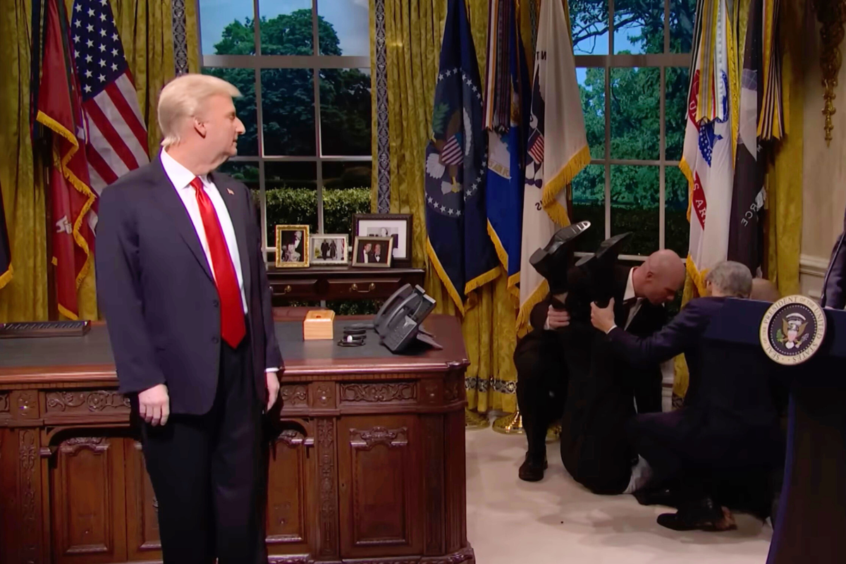 Left, James Austin Johnson on SNL as Donald Trump, turning to his left to look behind him at several men tending to a man on the floor on the right, lifting his feet in the air.