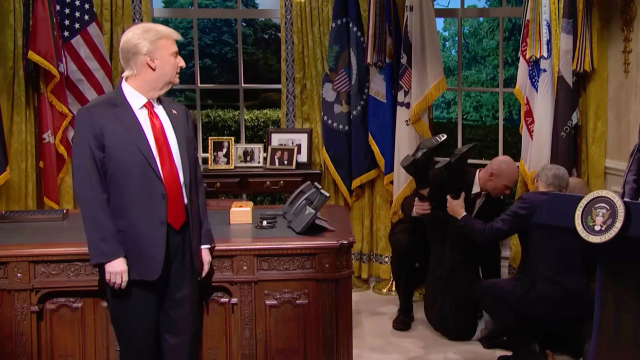 Left, James Austin Johnson on SNL as Donald Trump, turning to his left to look behind him at several men tending to a man on the floor on the right, lifting his feet in the air.