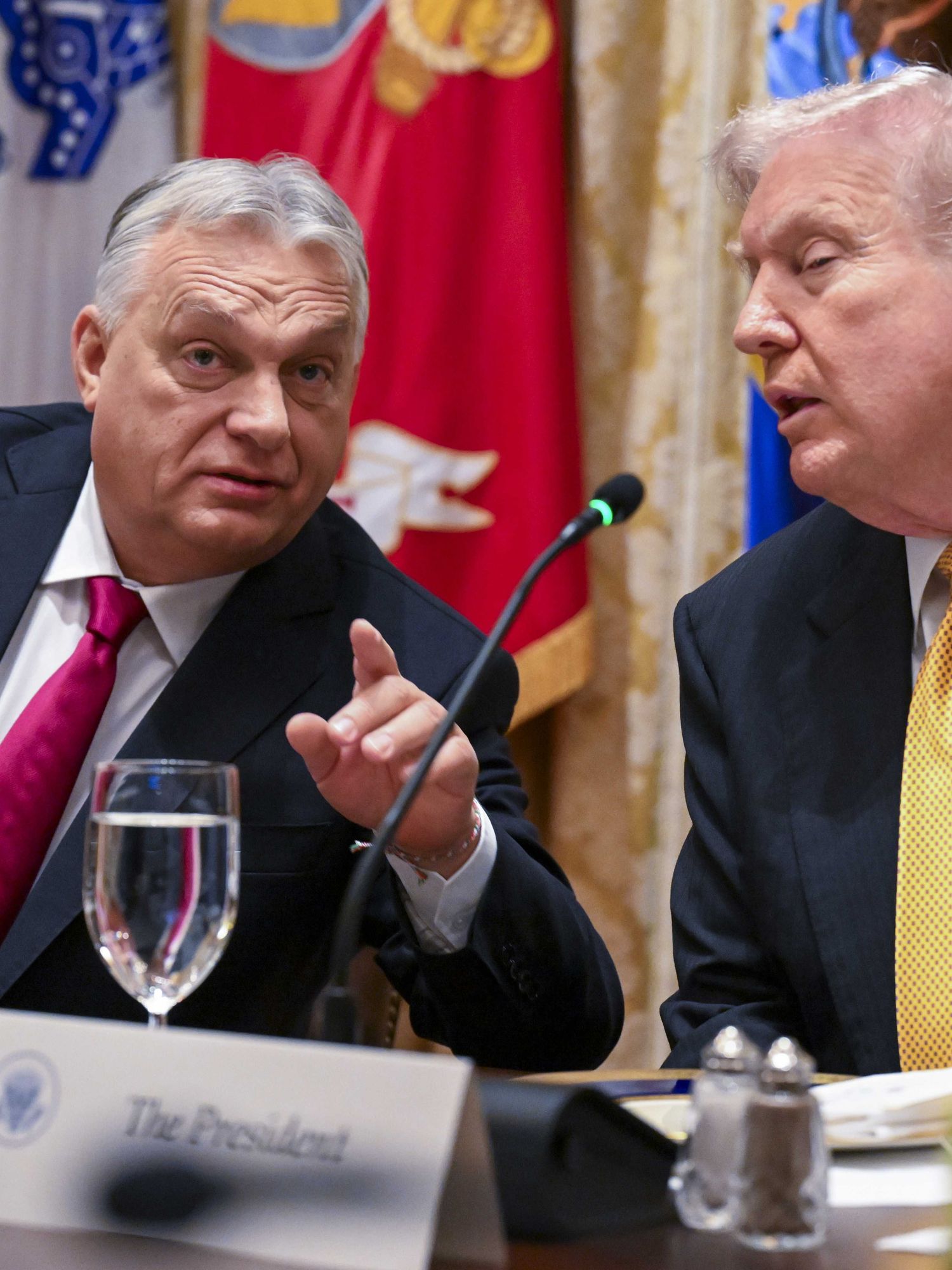 Left, Viktor Orbán points at someone off-camera in front of him. Right, US president Donald Trump listens. They are both sat at a wooden desk.