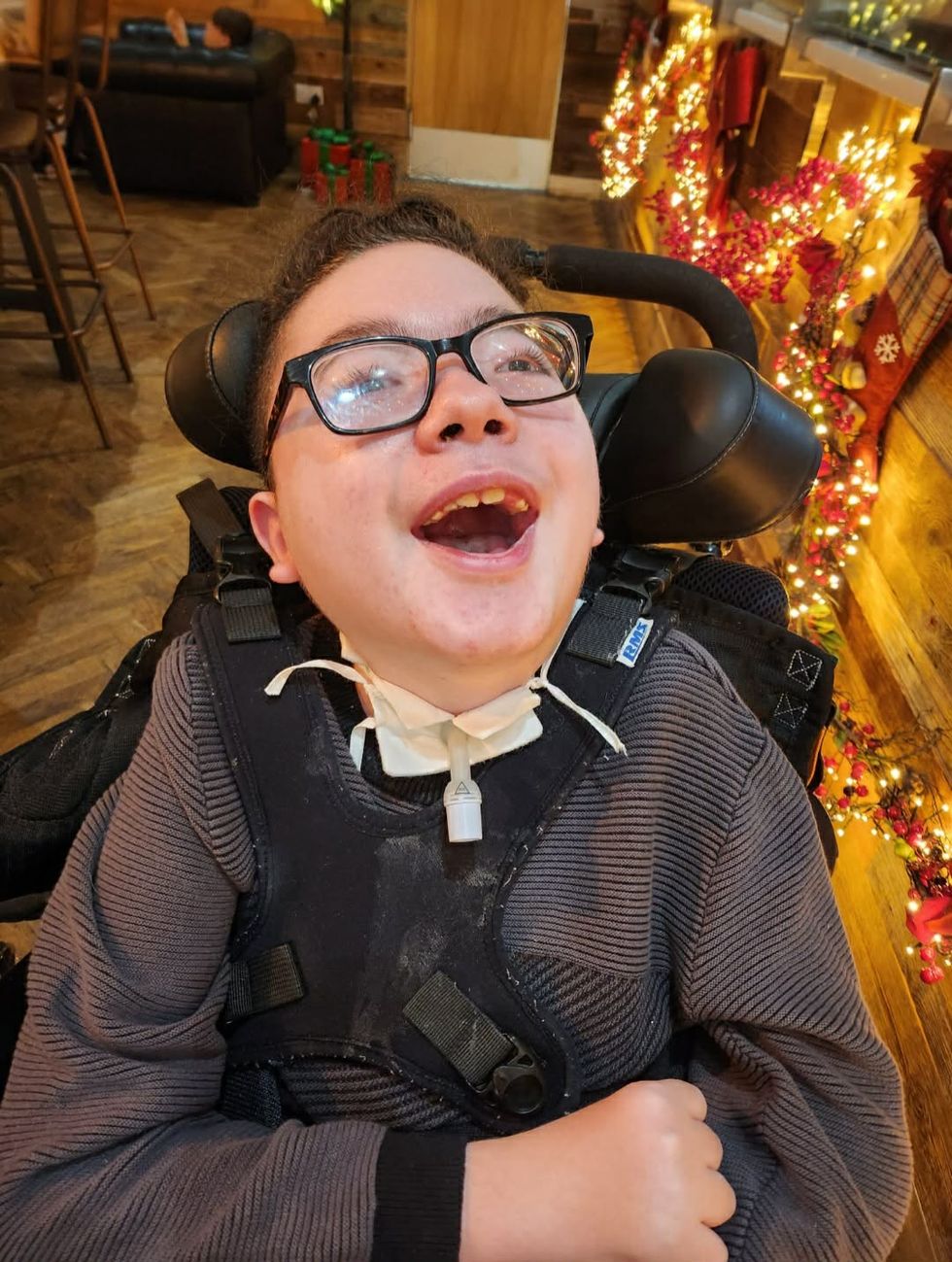 Liam smiling while in a wheelchair, in front of Christmas lights
