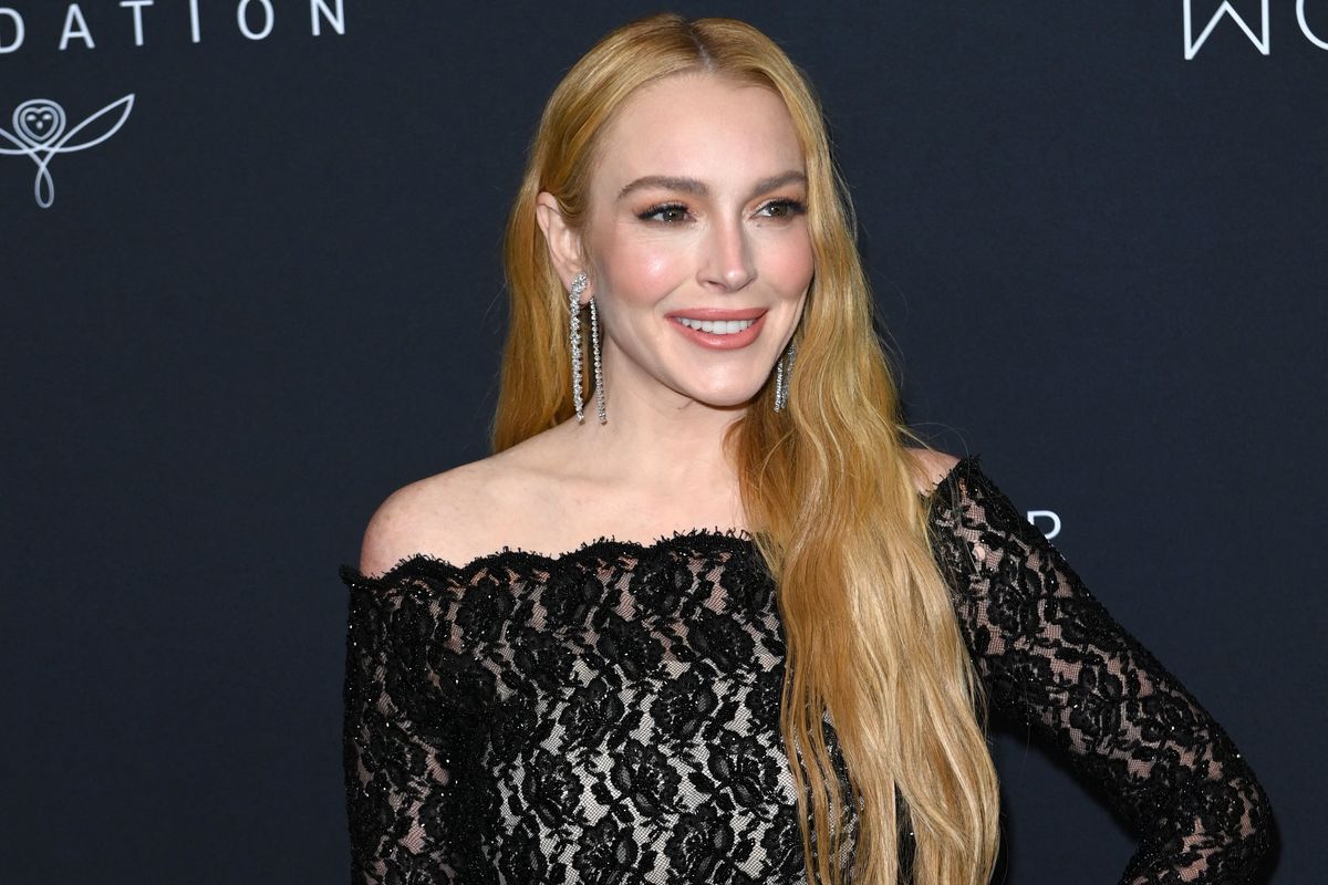 Lindsay Lohan wears a black lace dress and smiles at the camera as she poses at a Kering charity gala