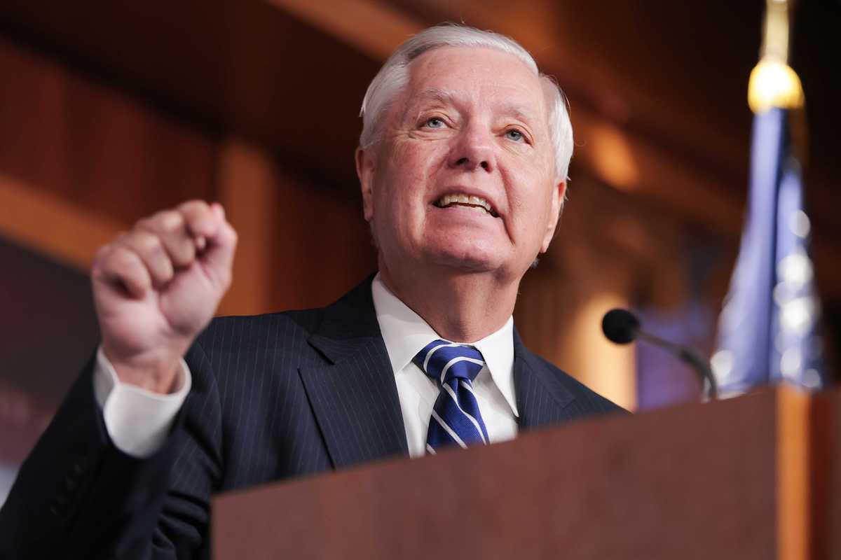 Lindsey Graham, a white man with short white hair, speaks behind a wooden lectern with his right fist clenched.