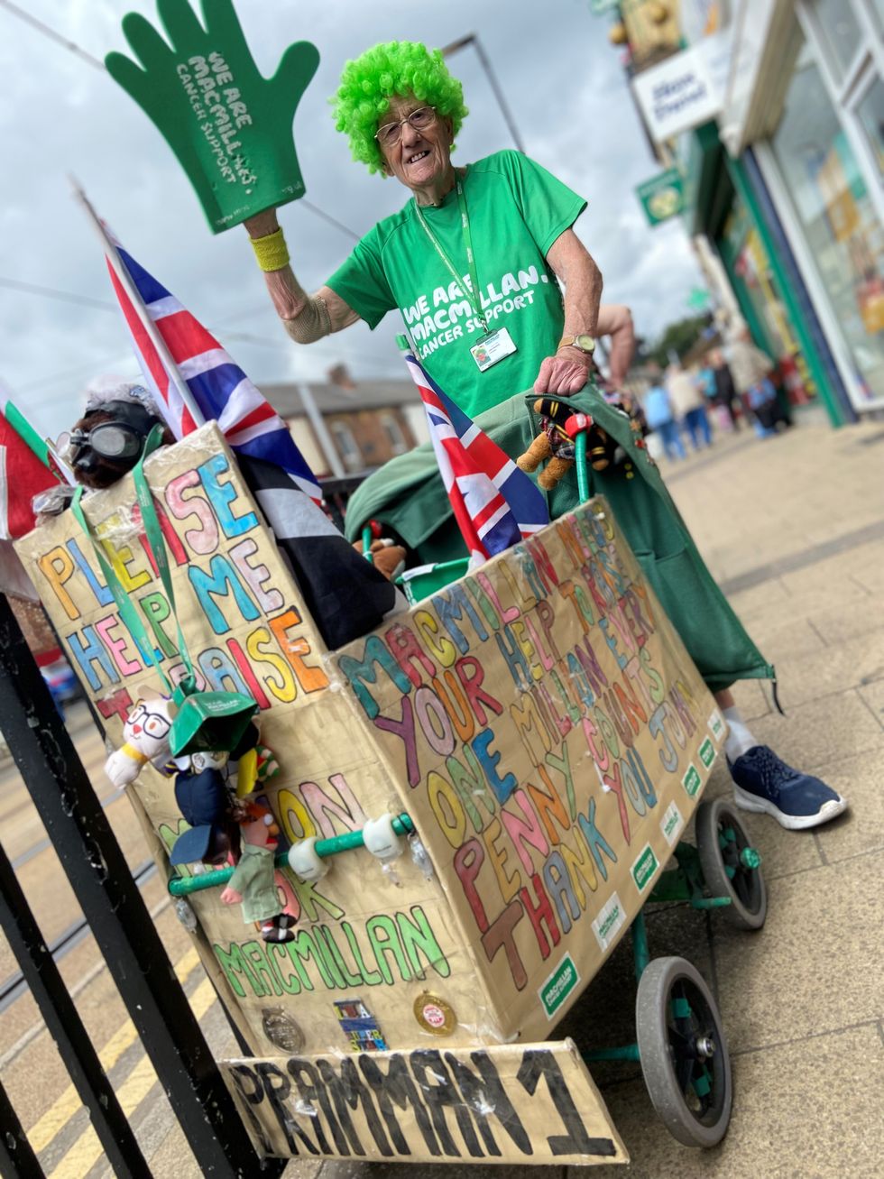 Man dressed in green with a giant green hand pushing a pram
