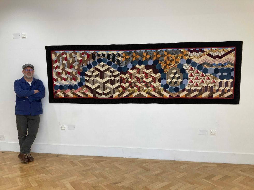Man posing next to quilt on wall