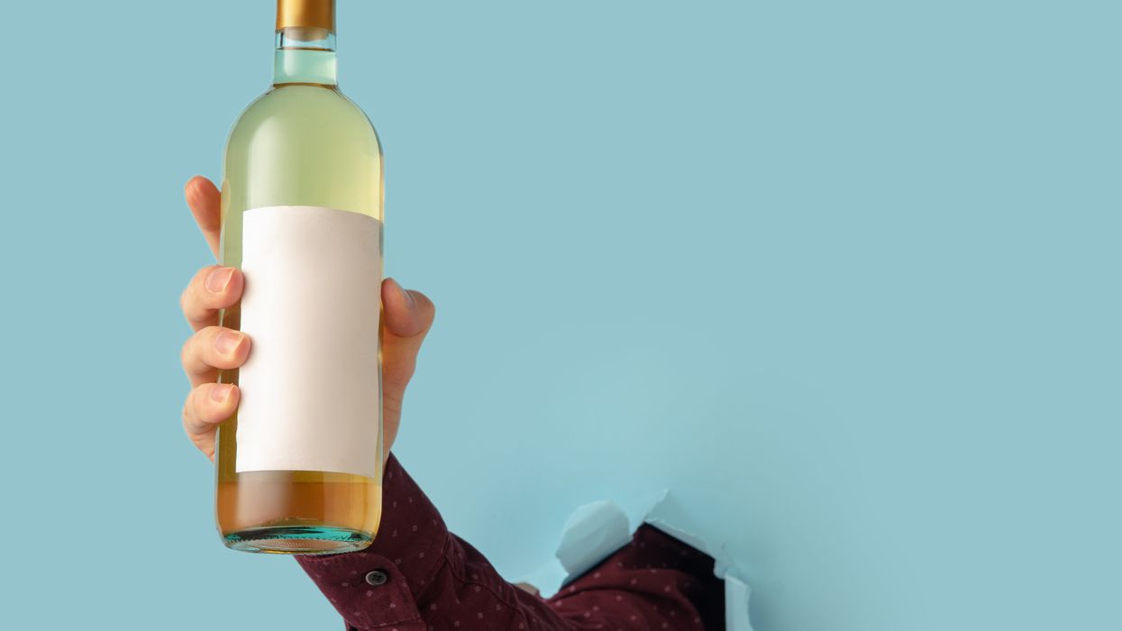 <p>Man's hand holding bottle of wine and breaking through blue paper background.</p>