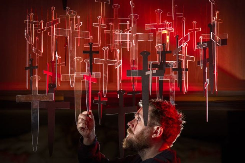 Man touching an exhibition of crosses in front of a red background