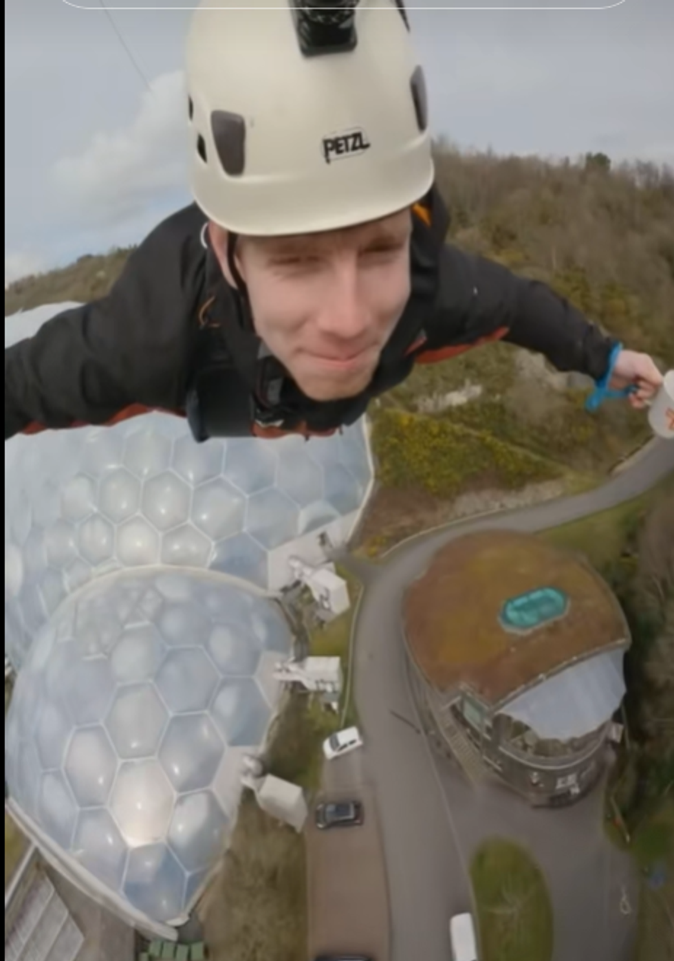 Man ziplining over the Eden Project in Cornwall with arm outstretched while holding a cup of tea