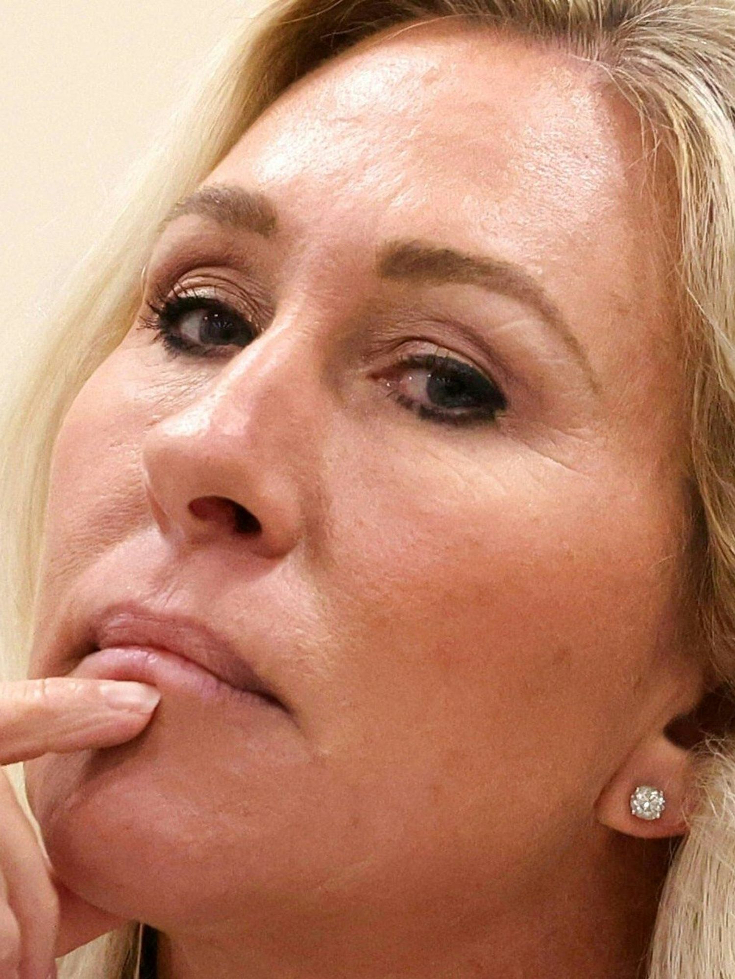Marjorie Taylor Greene, a white woman with long blonde hair, places her index finger on her chin, in thought, with her head tilted back slightly.