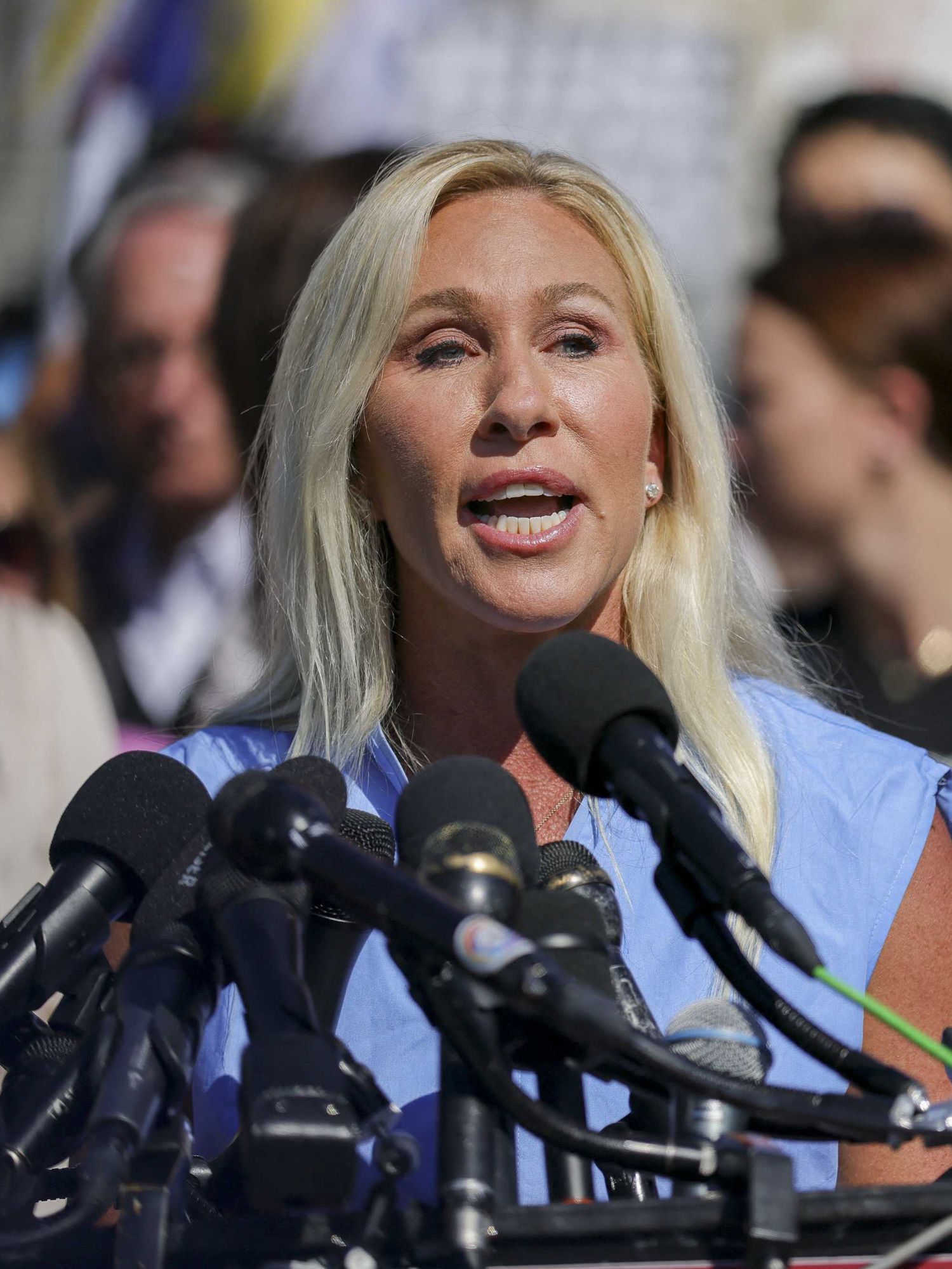 Marjorie Taylor Greene speaking into several microphones at a media event outside the Capitol.