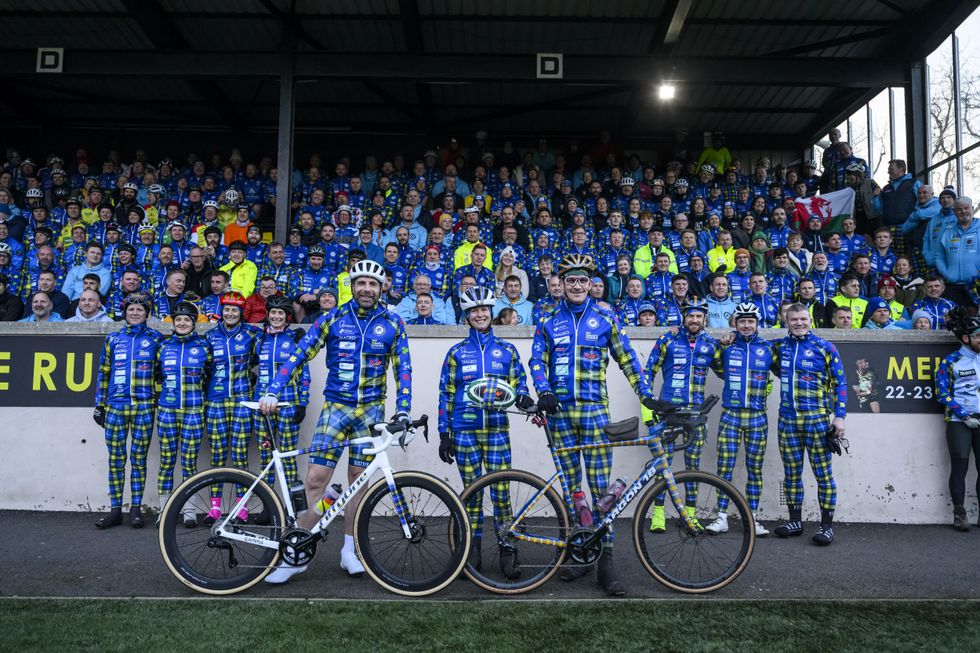 Mark Beaumont, Rob Wainwright and Kathy Weir dressed in blue and yellow tartan cycling gear with bikes, in front of a stand full of people in the same colours