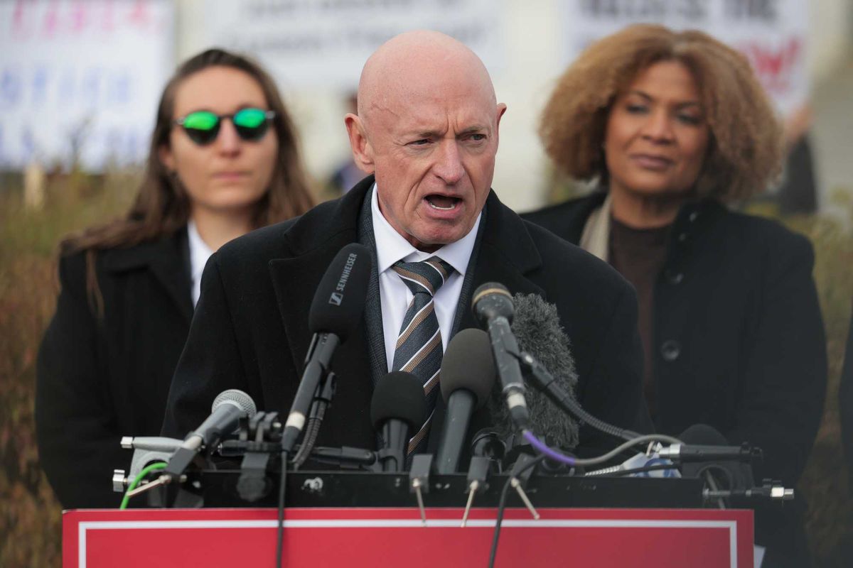Mark Kelly, a bald white man, speaking into several microphones on a lectern.