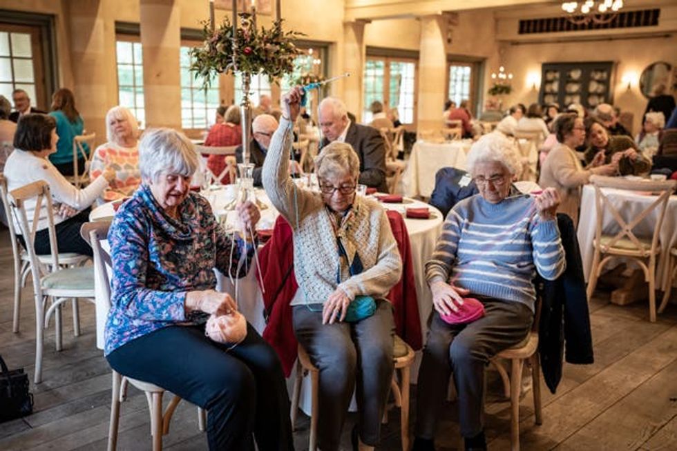 Marlene Ash, Dianne King, and May Keylock sit with balls of wool on their laps while knitting at the Winter Warmers event in the Orchard Room